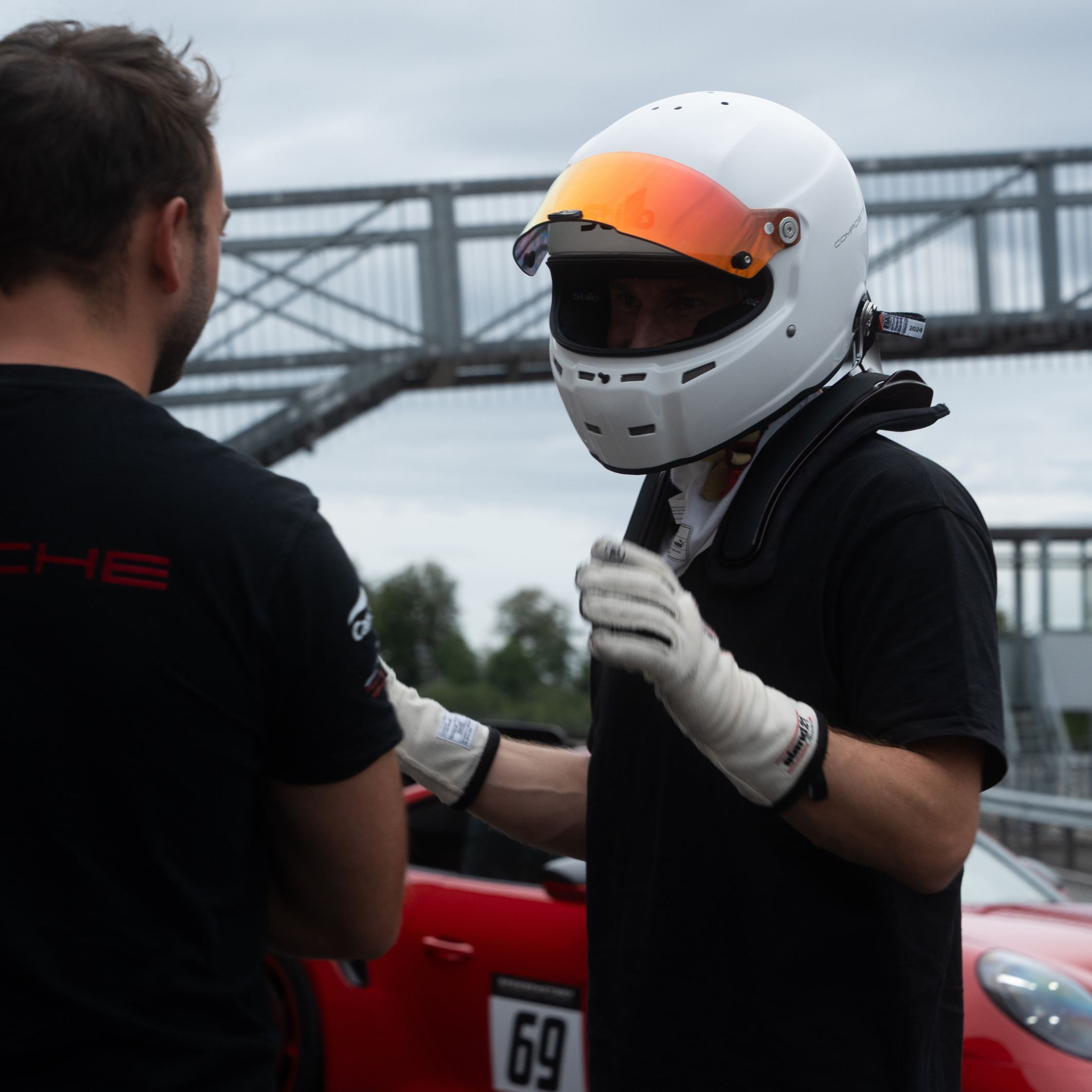 Fahrer mit Helm und HANS-Device neben einem Porsche GT3 RS